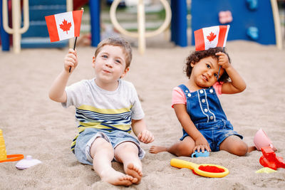 Portrait of boy and girl holding flags while playing with toys on sand