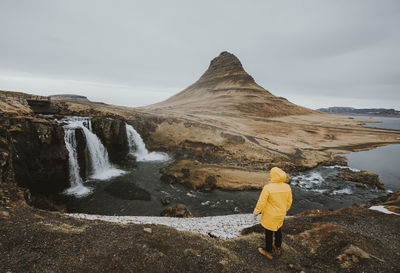 Rear view of man standing on rock against mountain and sky