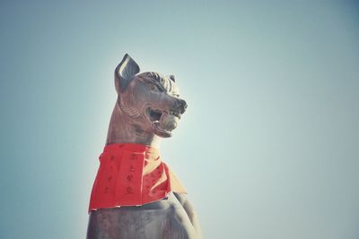 Low angle view of fox sculpture at fushimi inari taisha shrine against clear sky