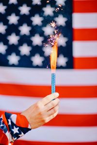 Cropped hand holding lit firework against american flag