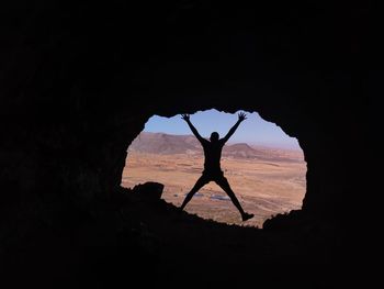 Silhouette man standing on rock against sky