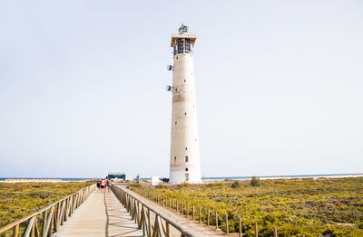 People walking on road by lighthouse against clear sky