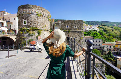 Back view of beautiful woman in pizzo with murat aragon castle in pizzo, calabria, italy.