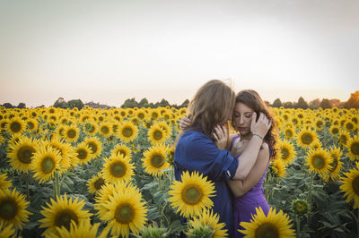 Rear view of mother and girl on sunflower field against clear sky