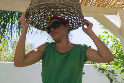 Low angle view of woman holding basket while standing against sky