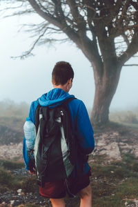 Back view of active touristic person in blue jacket and backpack climbing on ill with dry orange vegetation in spain