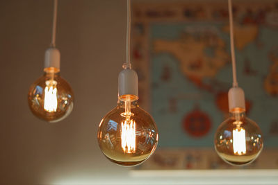 Close-up of illuminated light bulb hanging against wall