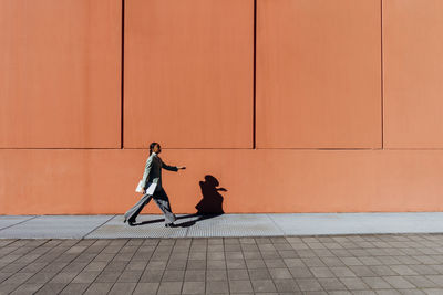 Businesswoman with laptop walking by orange wall