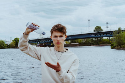 Portrait of confident man pouring water from bottle against sky