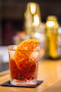 Shot of a negroni cocktail with orange garnish and unfocused background of the bar
