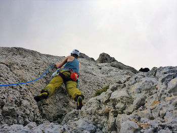 Rear view of person climbing rock on mountain against sky