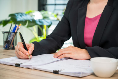 Midsection of woman holding paper while sitting on table