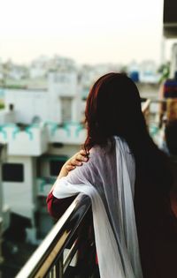 Rear view of teenager girl standing by railing in city