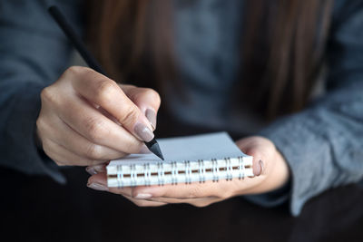 Midsection of woman writing on spiral notebook with pencil