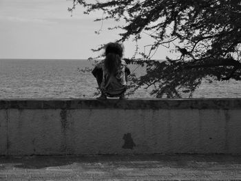 Rear view of girl crouching on retaining wall against sea