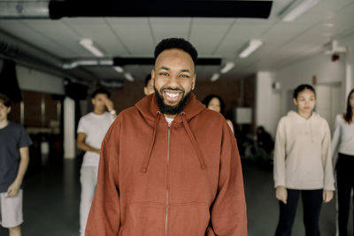 Portrait of happy male teacher with students in background at dance studio