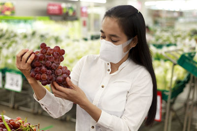 Close-up of woman wearing mask holding grapes