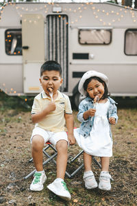Asian multiracial kids girl and boy eat meat on a barbecue on a picnic in woods in summer on a trip