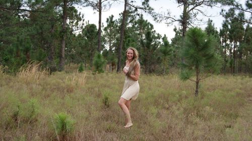 Beautiful blond woman dancing on grassy field against trees at forest