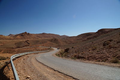 Road leading towards mountains against clear blue sky