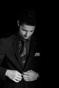 Young man wearing suit standing against black background