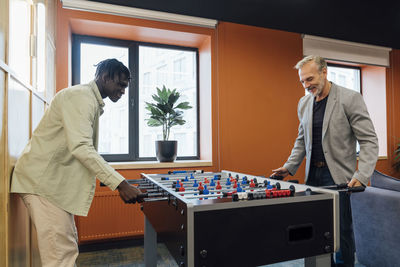 Smiling businessman playing foosball with colleague in office