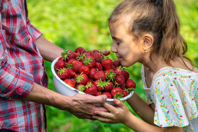 Girl smelling fresh strawberries in bowl holding by man