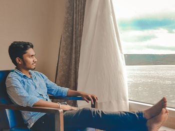 Young man looking away while sitting on railing