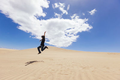 Man jumping on sand at desert against sky