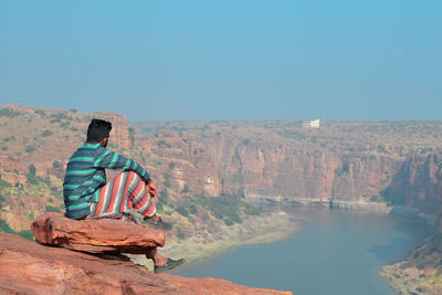 Man sitting on rock against sky