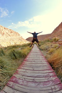 Full length of man over wooden walkway on grassy field against sky