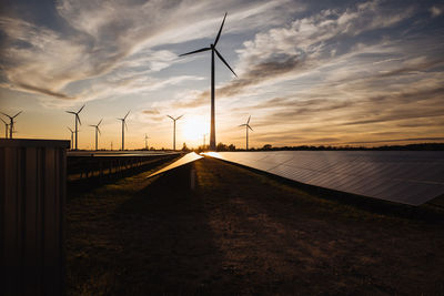 Scenic view of turbines and solar panels against sky during sunset