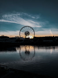 Silhouette ferris wheel by lake against sky during sunset