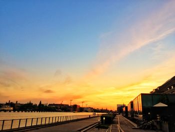 Road by buildings against sky during sunset