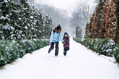 Happy family, mother, son and cat in backpack walking on the snowy alley in winter snowy nature