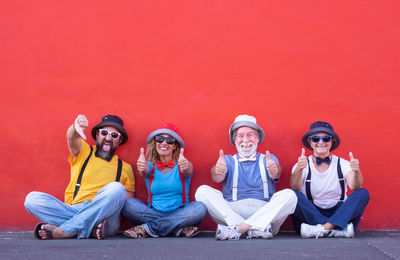 Portrait of family sitting while showing thumbs up against red wall