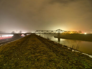 Illuminated bridge over river against sky at sunset