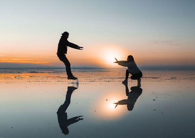 Silhouette couple enjoying at beach against sky during sunset