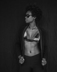Young woman wearing sunglasses and bra standing against wall