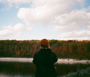 Rear view of man standing by lake against sky