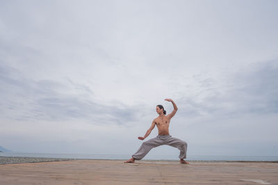 Full length of young woman doing yoga at beach against sky