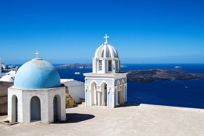 Church by sea against clear blue sky on sunny day