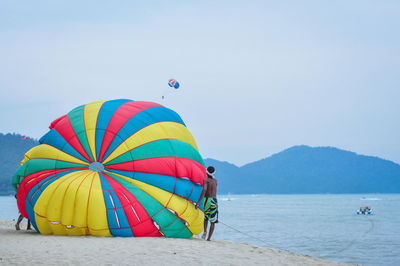 Man with parachute standing at beach against sky