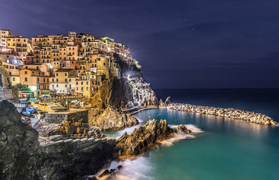 Panoramic shot of illuminated buildings by sea against sky