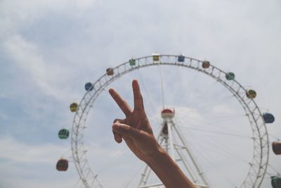 Cropped image of woman gesturing peace sign against ferris wheel