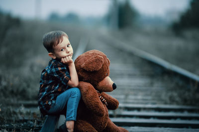 Boy with teddy bear sitting on railroad track