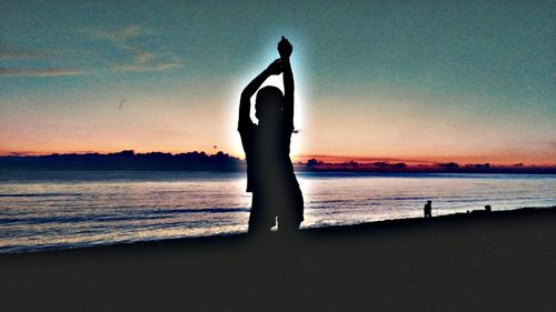 Silhouette woman standing on beach against sky during sunset