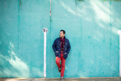 Bearded man in casual clothes leaning on green wall while looking away outdoors