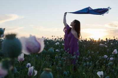 Rear view of woman standing on field against sky during sunset