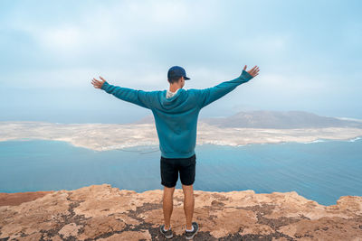 Rear view of man with arms outstretched standing on cliff